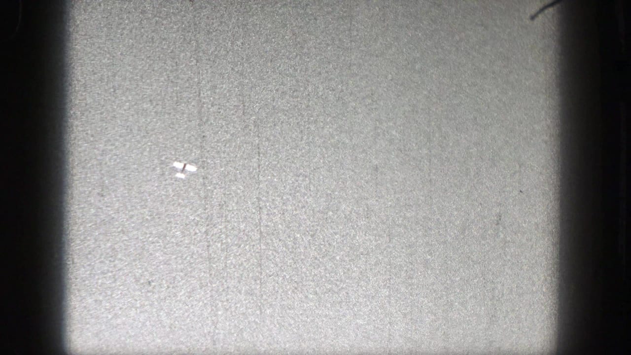 Tiny pale aircraft-like shape near the center of a grainy sky frame.