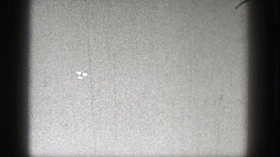 A tiny pale object resembling a model plane is visible against the grainy sky, with dark 8mm frame borders.