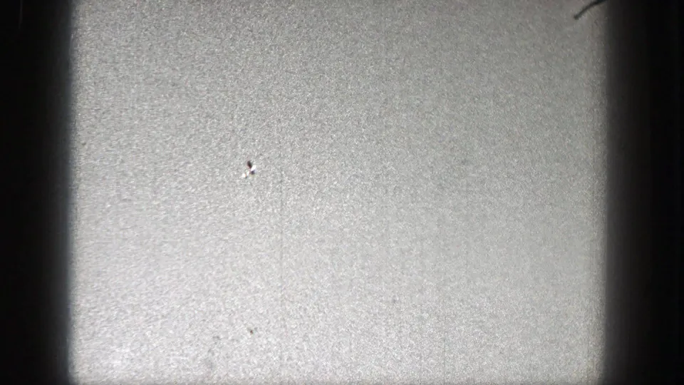 The frame shows mostly pale grainy sky, a small bright speck, and dark rounded edges from the scanned 8mm film.
