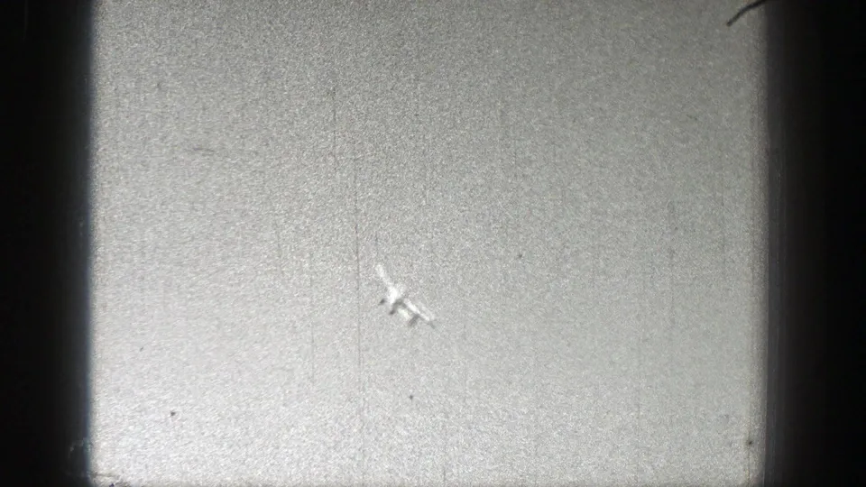A small model airplane appears near the ground in the dusty field, with film scratches and vignetting visible around the frame.