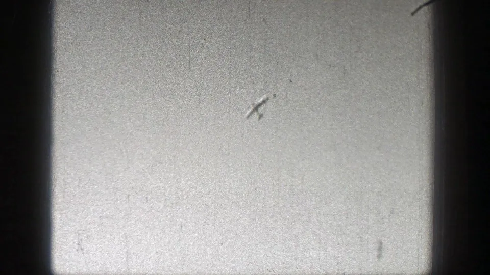 A distant aircraft is seen against a bright sky in soft, scratched 8mm footage from the 1938 Washington clip.