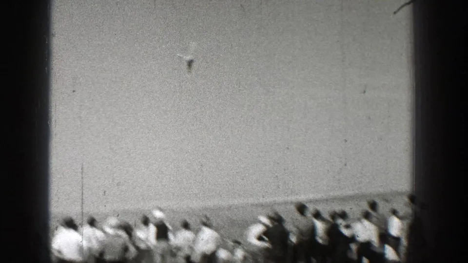 A distant aircraft flies above a line of spectators in a flat open field, consistent with the 1938 Washington home-movie metadata.