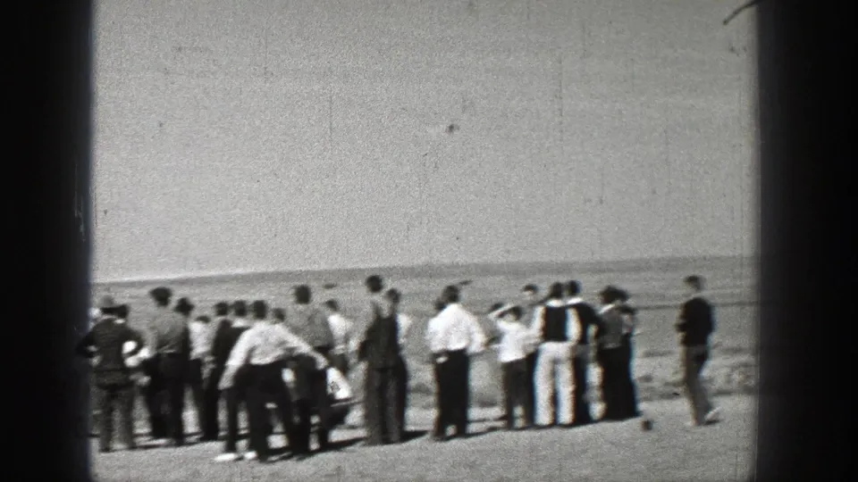 Washington 1938 home-movie frame showing spectators in period clothing gathered in an open field, watching the sky.