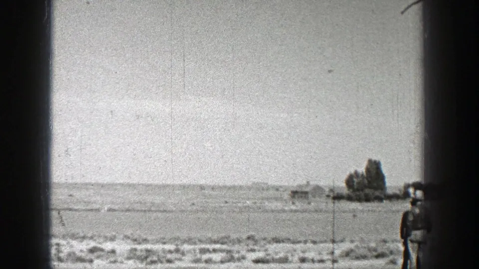 Washington 1938 frame showing open scrubland, a distant horizon, a small structure or object, trees, and one spectator near the frame edge.