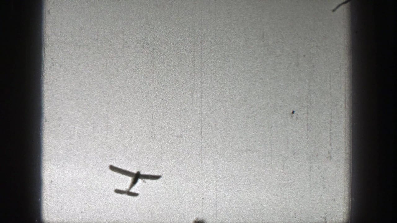 Small light aircraft seen from below against a bright sky in 1938 Washington home-movie footage.