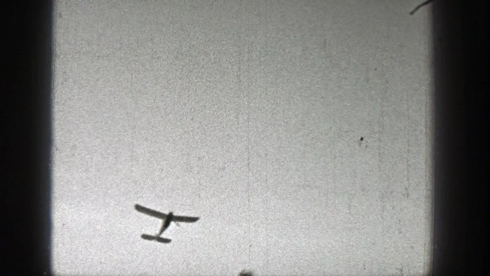 Small light aircraft seen from below against a bright sky in 1938 Washington home-movie footage.