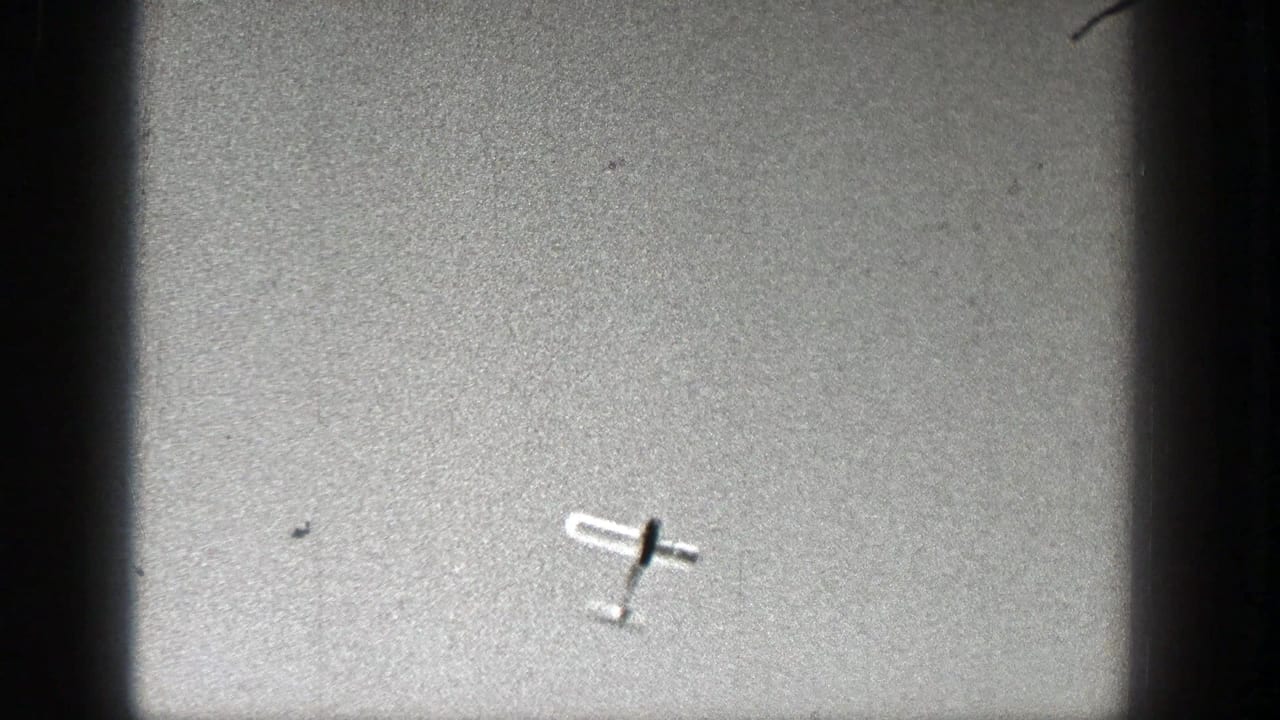 Light aircraft angled against an overcast sky with visible film wear.
