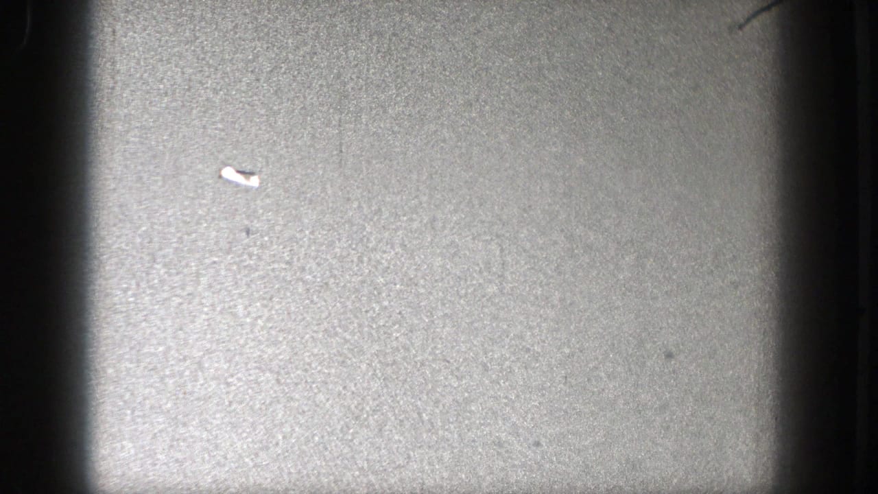 Small bright aircraft mark in open sky with central dark film band.