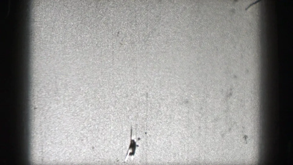 A small aircraft form appears lower in the frame, with 8mm grain, scratches, and shadowed frame edges surrounding the sky.