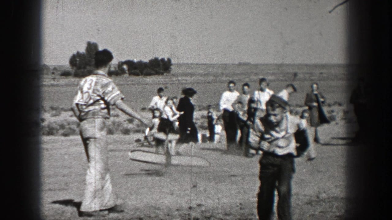 1938 Washington home-movie frame showing people crossing an open walkway or roadside area, with distant trees and soft 8mm grain.
