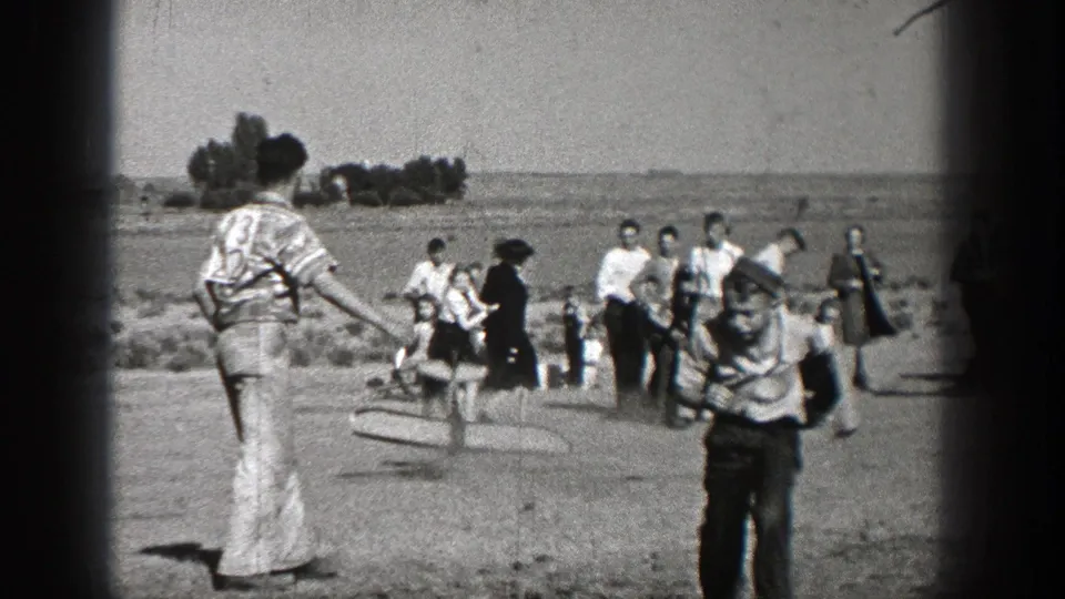 1938 Washington home-movie frame showing people crossing an open walkway or roadside area, with distant trees and soft 8mm grain.