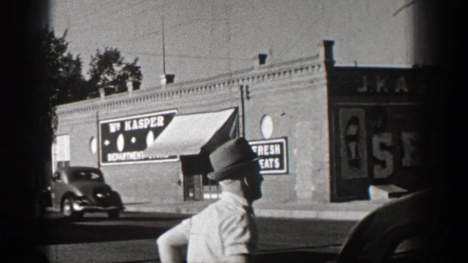 1938 Washington street frame with a fedora-wearing man, a rounded automobile, and a visible W. Kasper department-store sign.