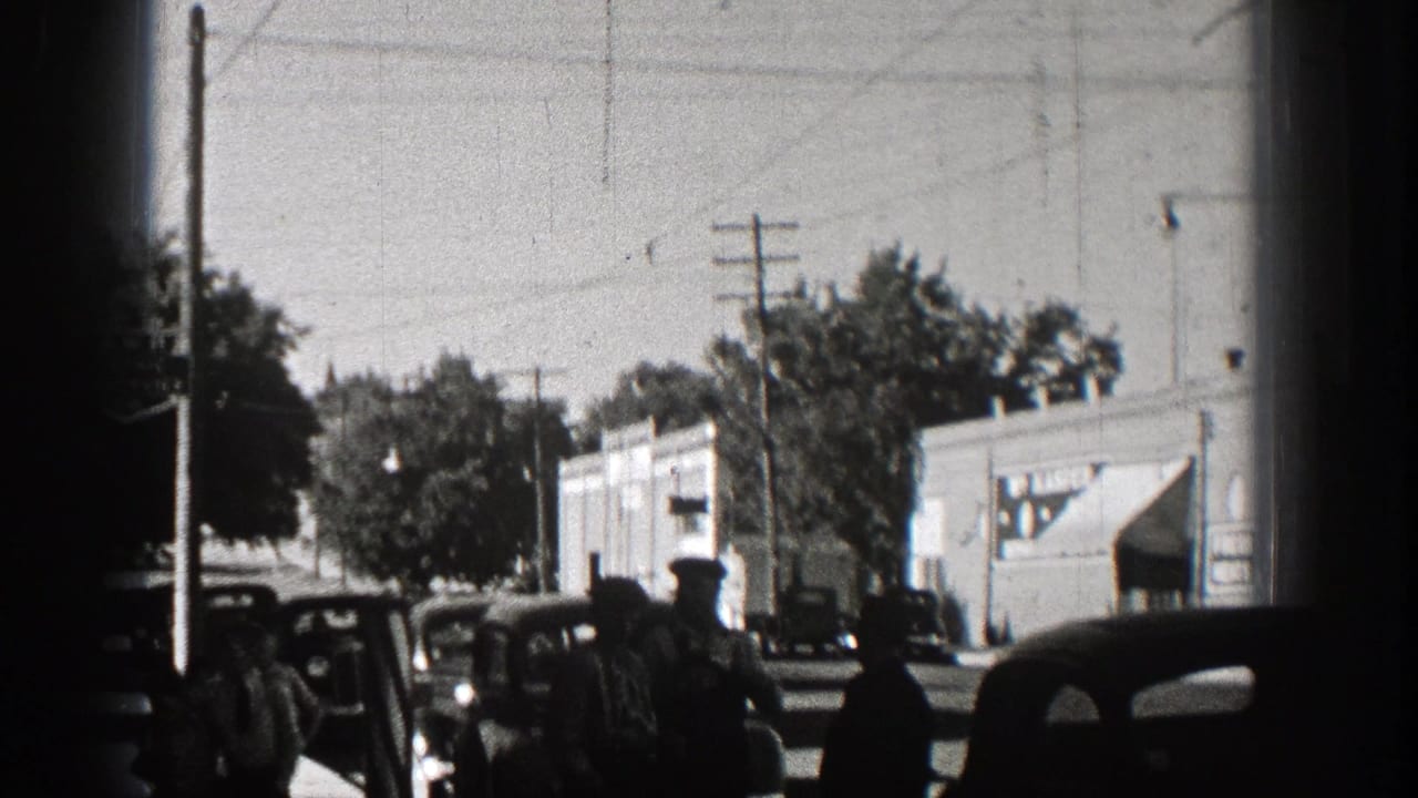1938 Washington street scene with men near dark vintage cars, utility poles, trees, and storefront or commercial buildings.