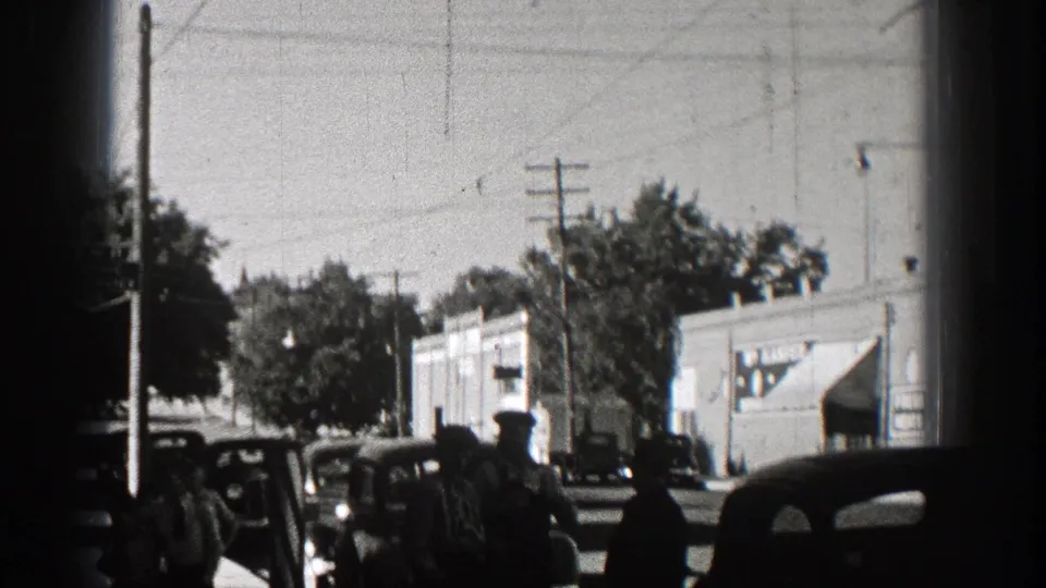 1938 Washington street scene with men near dark vintage cars, utility poles, trees, and storefront or commercial buildings.