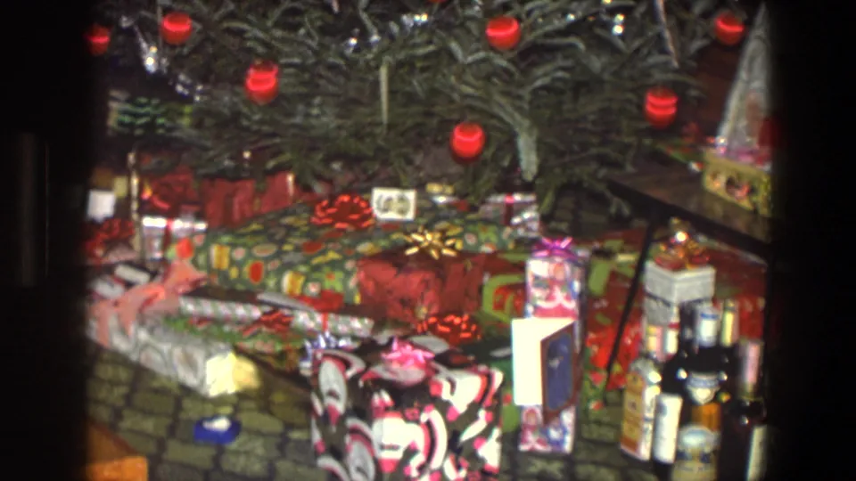 Wrapped Christmas gifts beneath the decorated tree in 1971 Saint Paul home-movie footage, with patterned paper, ribbons, and ornaments visible.