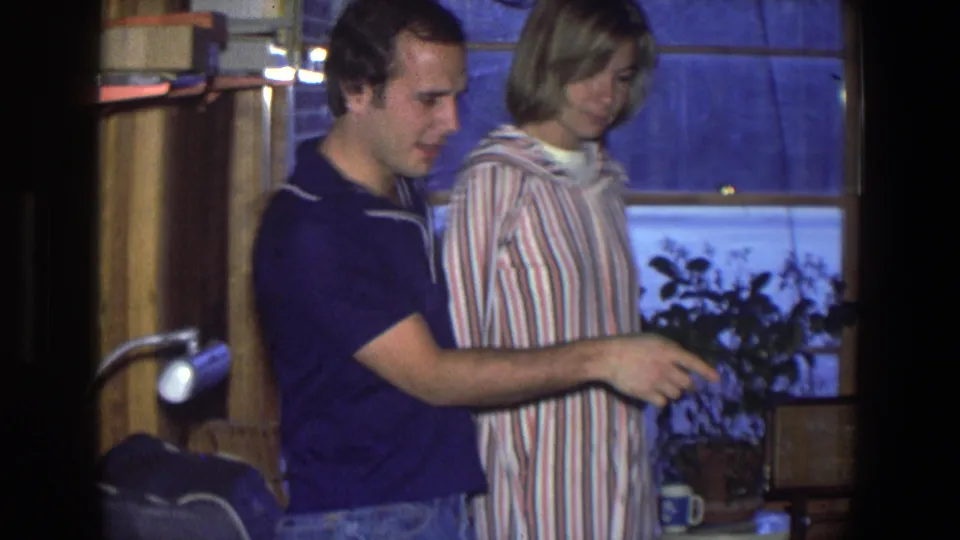 In a 1971 Saint Paul home interior, a couple stands close together near a snowy window and potted plant.