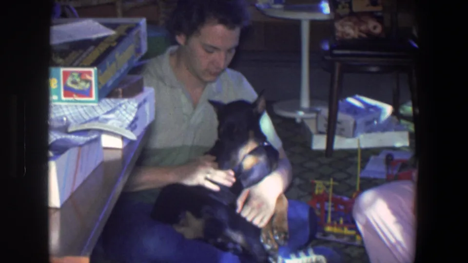 The young man in the green shirt looks down at the black and brown puppy in the Saint Paul home interior, with toys and papers nearby.