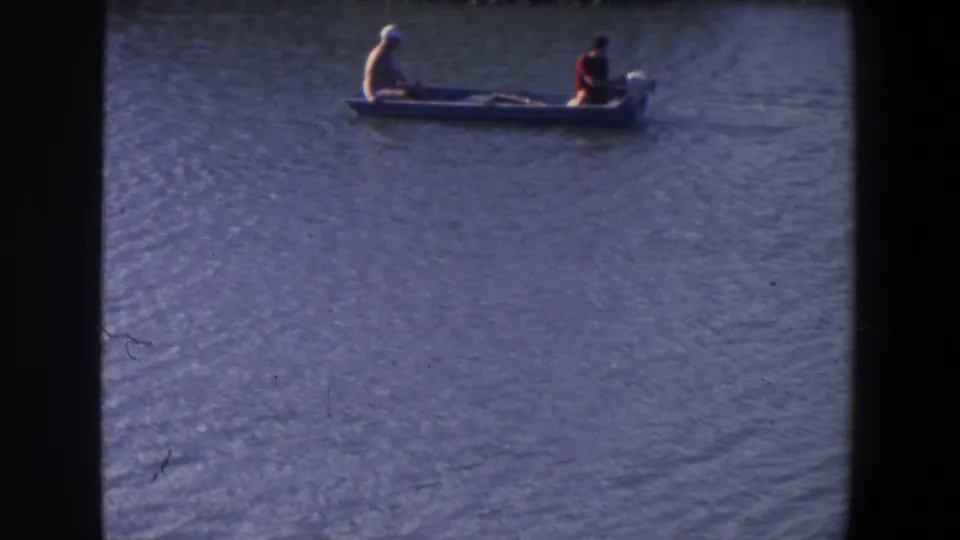 In 1971 Saint Paul home-movie footage, two people ride in a small open motorboat across calm, rippled water.