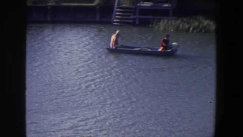 The motorboat passes a dock or shoreline structure in Saint Paul, with one person in light clothing and another in a red shirt.