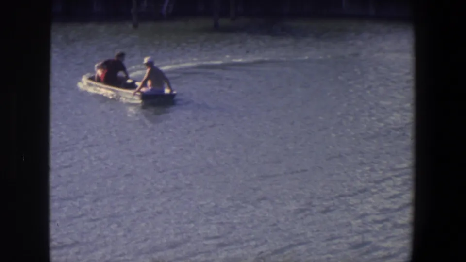 Two people in a small motorboat move across calm water in 1971 Saint Paul, Minnesota home-movie footage.