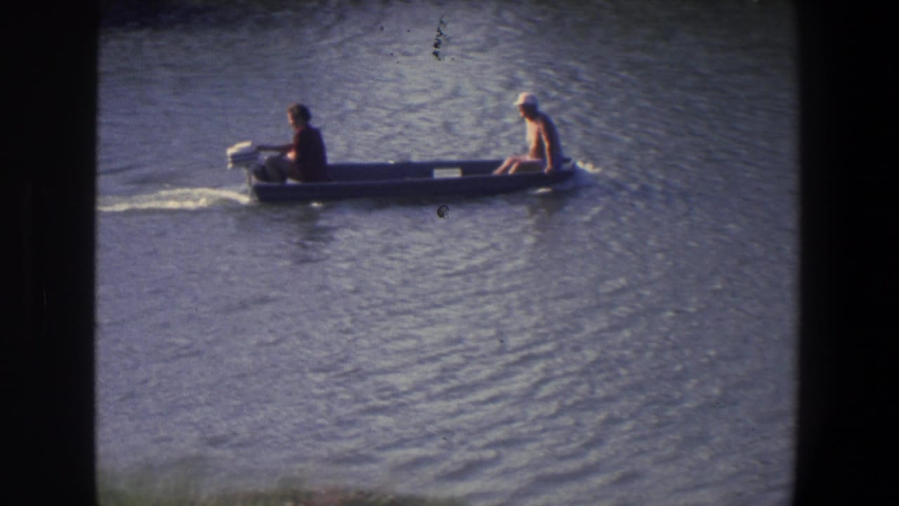 Two men ride in a small gray motorboat across rippled water.