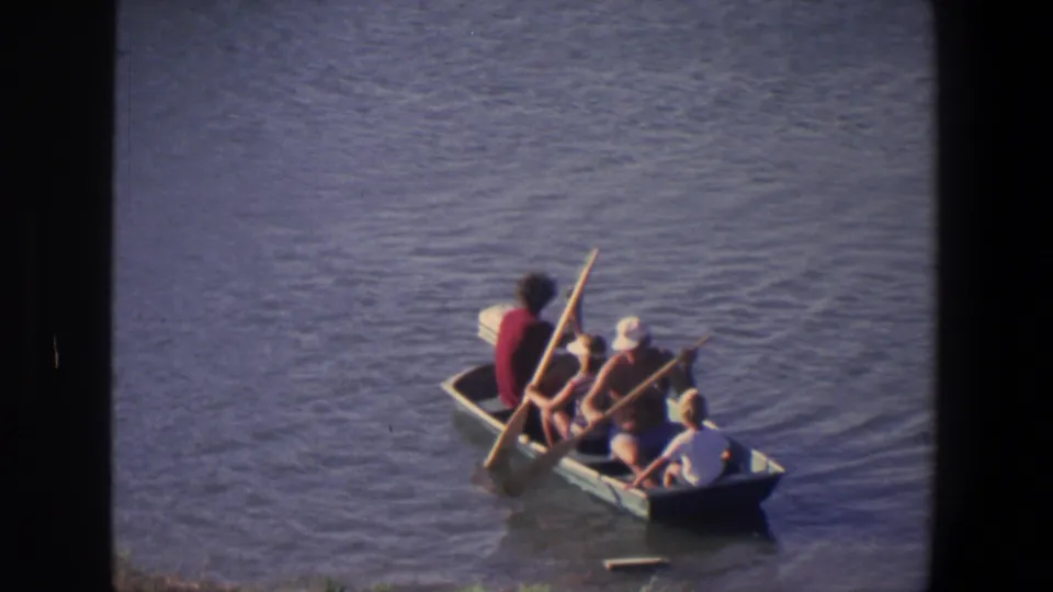 A small boat carries several people on the water, with one person in a red top and an oar visible near the stern.