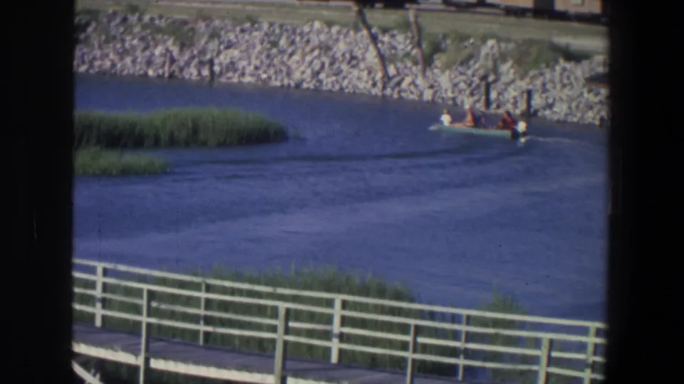 1971 Saint Paul river footage frame showing a small boat near reeds, with boardwalk rails and film contact borders visible.