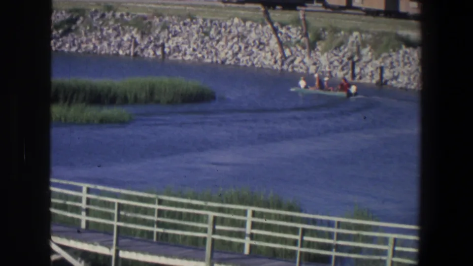 1971 Saint Paul 8mm frame showing a small motorboat carrying people past reeds, with a white waterfront railing in the foreground.
