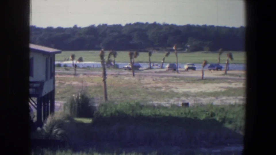 1971 home-movie frame identified as Saint Paul, Minnesota, with the waterside building partly cropped and cars visible across the grassy bank.