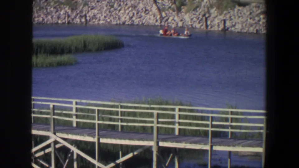 1971 Saint Paul 8mm frame showing a red-toned motorboat with passengers moving across the channel above a white dock.