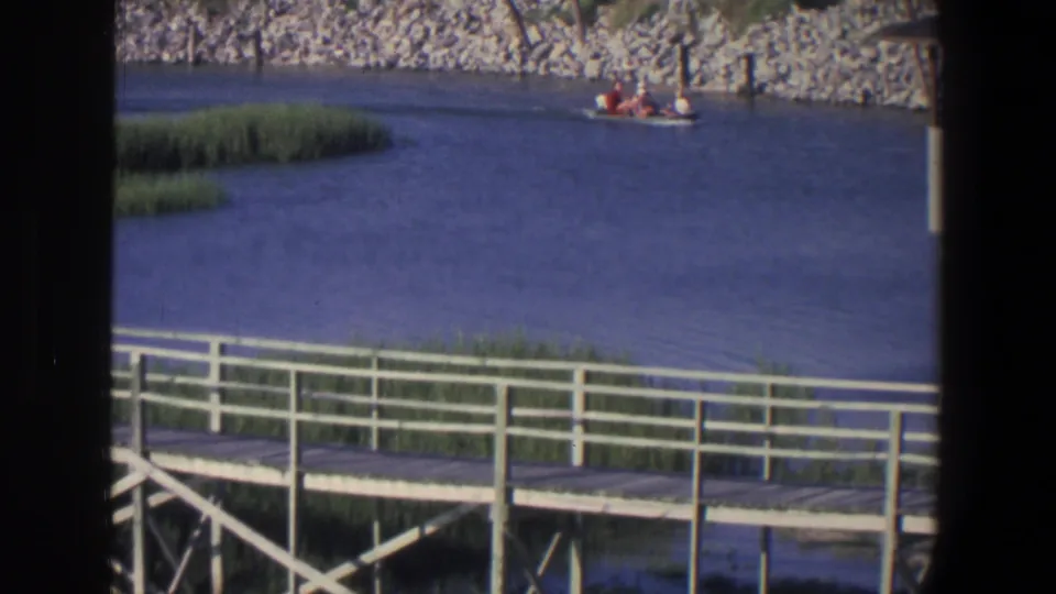 Late-frame 1971 Saint Paul view of a small motorboat near the rocky shore, with dock rails, reeds, and blue water below.