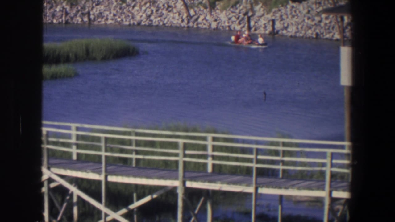 Small boat on a river beyond a wooden boardwalk with white railings and reeds.