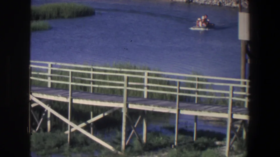 Small passenger boat on a Saint Paul river scene, seen from behind a white-railed wooden boardwalk in 1971 8mm footage.