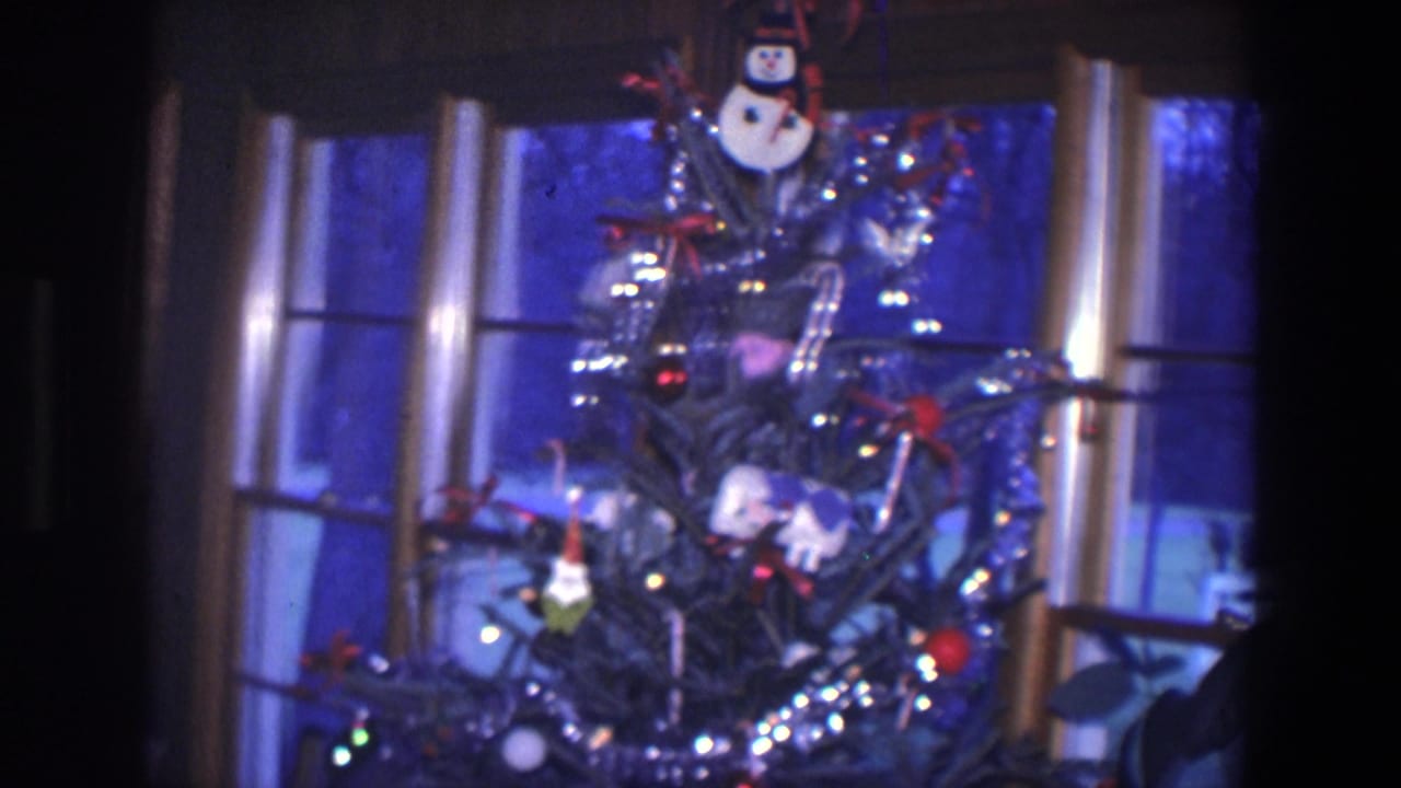 1971 Saint Paul home-movie frame showing a Christmas tree with tinsel, lights, ornaments, and a snowman decoration by a dark window.
