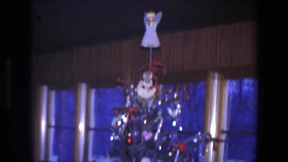 1971 Saint Paul home-movie view of the upper Christmas tree with a topper, snowman ornament, tinsel, and dark window panes behind it.