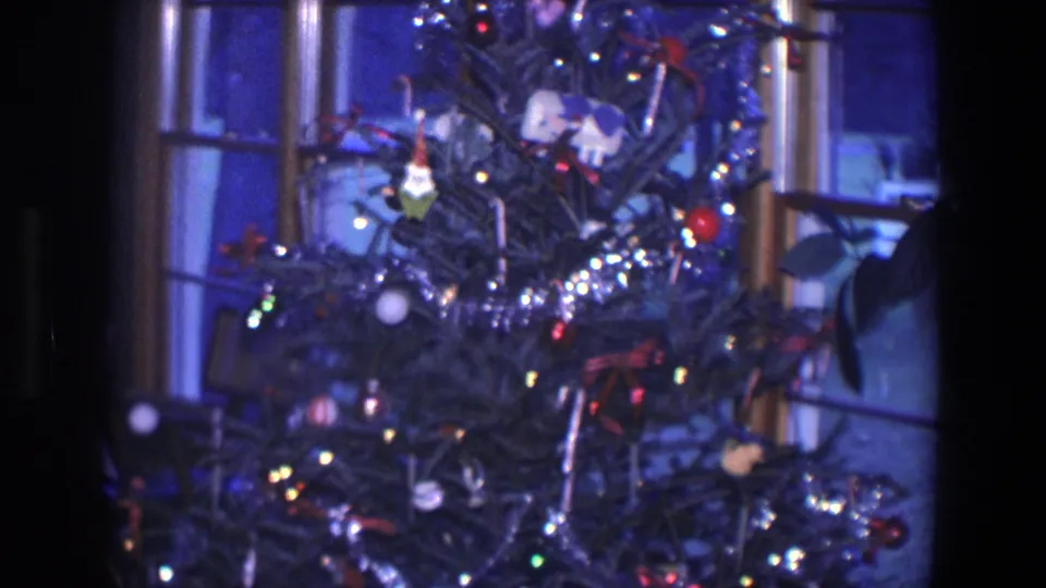 1971 Saint Paul home-movie frame focused on the middle of a Christmas tree with tinsel, small lights, ornaments, and window panes behind it.