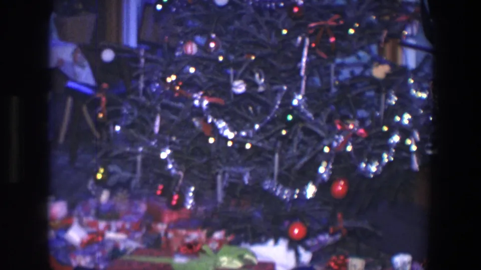 1971 Saint Paul home-movie view of the lower Christmas tree with tinsel, red ornaments, lights, and wrapped gifts at the base.
