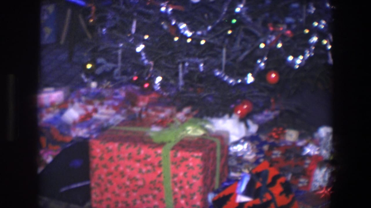 Christmas tree with tinsel and wrapped gifts on patterned carpet.