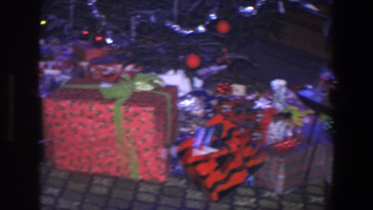 Large wrapped gift under a decorated Christmas tree with other presents nearby.