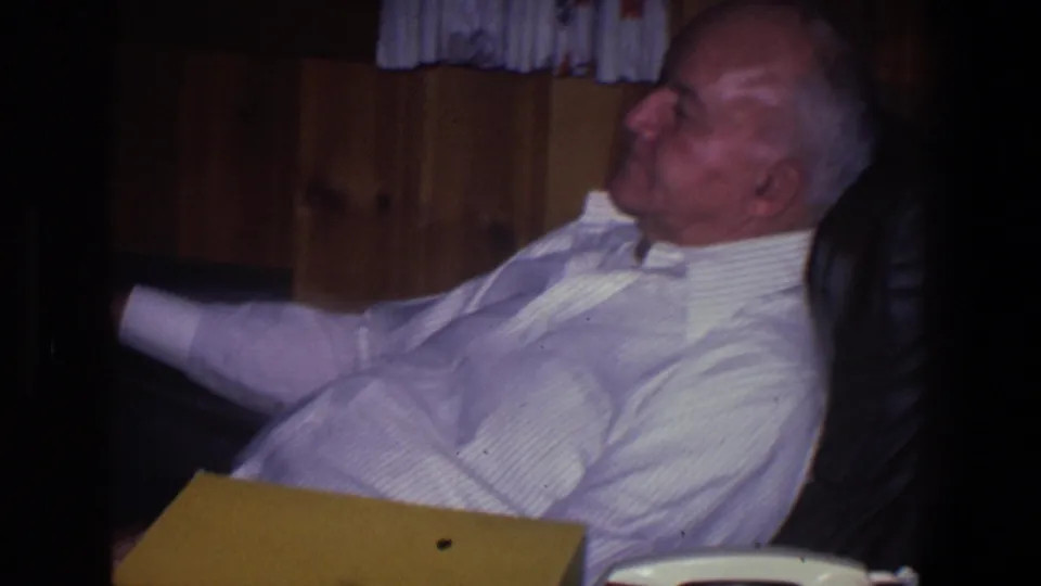 An older man in a light striped shirt reclines in a chair beside wood paneling and curtains in a 1971 Saint Paul home interior.