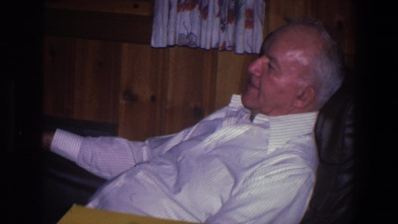 Elderly man in profile resting in a leather armchair against a wood-paneled wall.