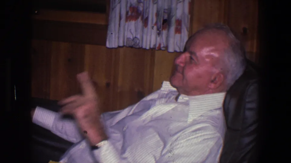 The Saint Paul home-movie frame catches the man gesturing with one hand while relaxed in the leather chair.