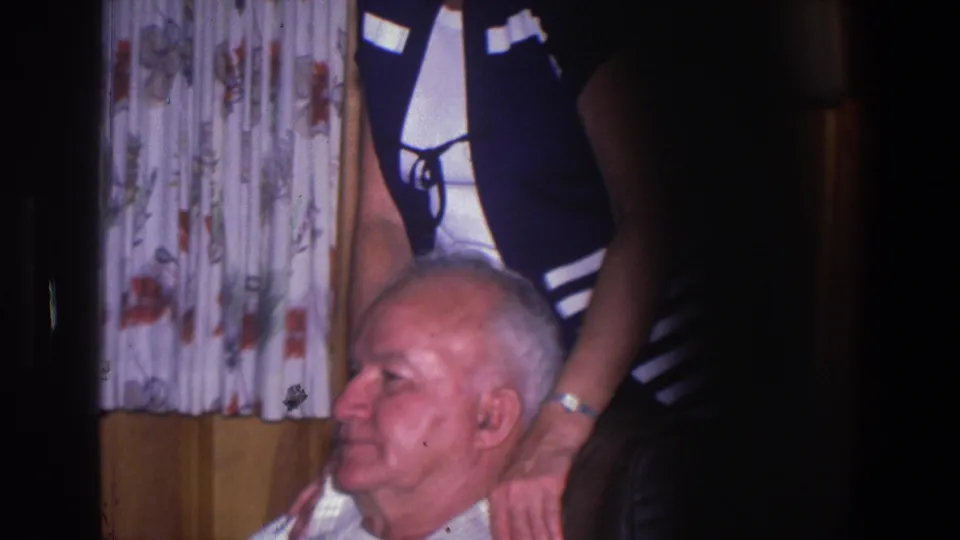 The older man sits in profile as the woman stands behind him with her hands near his shoulders in the 1971 home interior.