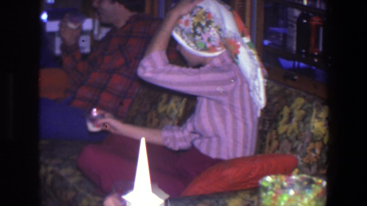 Adults seated on a patterned couch, with a woman in a pink striped top adjusting a floral headscarf.