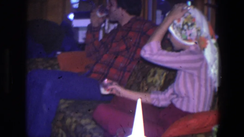 1971 Saint Paul home interior with adults on a patterned couch, including a woman in a pink striped top holding a glass near a floral headscarf.