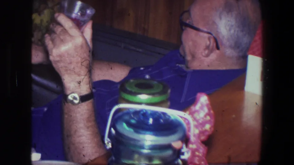 Profile view of an older man in glasses holding a drink in a 1971 Saint Paul wood-paneled room.