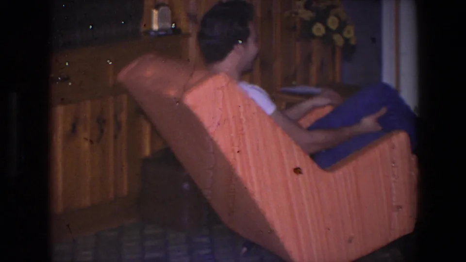Younger man relaxes in a striped orange armchair inside a 1971 Saint Paul home interior with wood paneling.