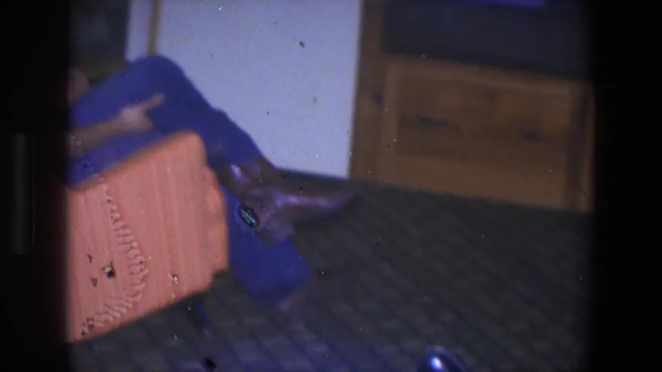 1971 Saint Paul home-movie frame showing a reclining figure in blue clothing near an orange chair and patterned floor.