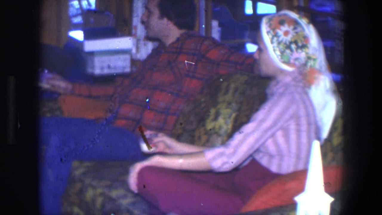 Couple seated on a patterned sofa, each holding a drink in a living room.