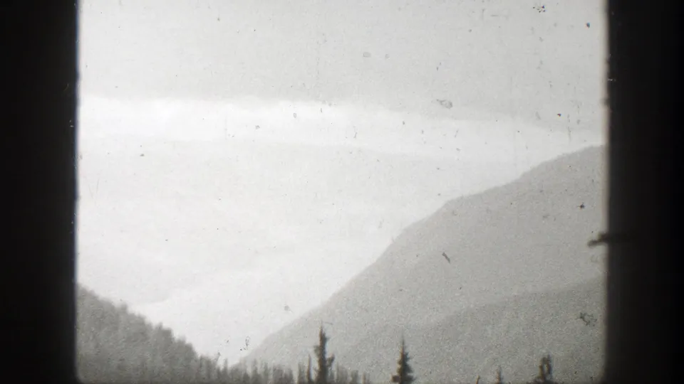 Soft black-and-white view of a California mountain valley with ridges and conifers in 1938 home-movie footage.